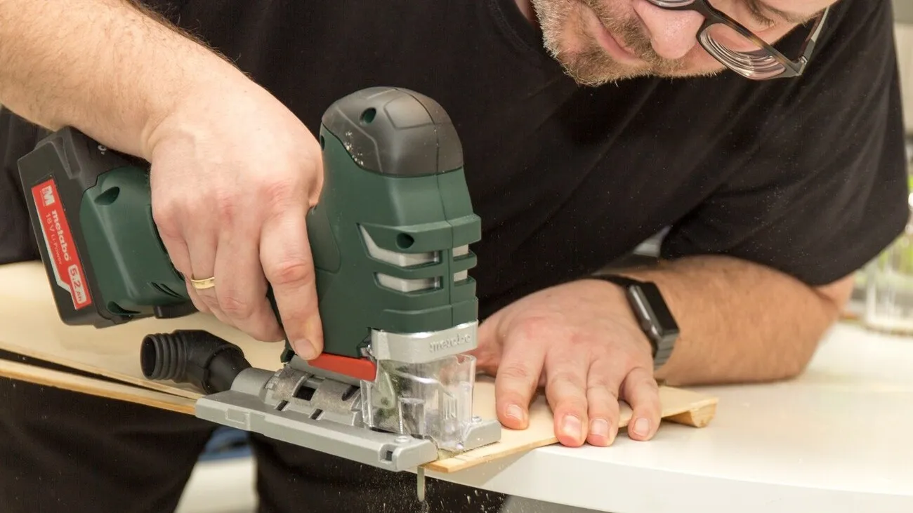 Ein Mann sägt mit der Metabo Stichsäge am Tischende eine Multiplexplatte.